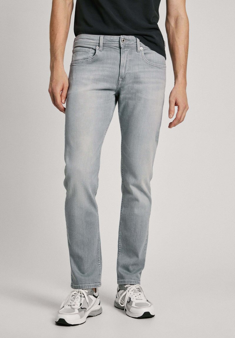 Jeans de denim gris claro con corte recto. Cuenta con cinco bolsillos, cierre de botón y cremallera, y un desgaste sutil. Combinados con zapatillas deportivas blancas.