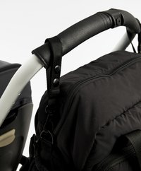Zaino in tessuto nero con texture imbottita e una zip prominente. Presenta una maniglia in pelle nera liscia e clip di attacco sui lati.