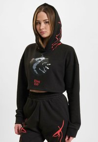 Black cropped hoodie with a wolf graphic and red "Thug Life" text. Features a hood, relaxed fit, and matching black pants with red accents.