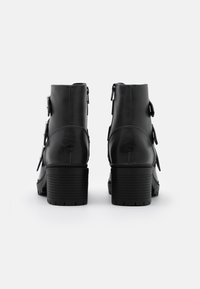 Botas negras hasta el tobillo con un acabado de cuero suave, con un tacón grueso, cremalleras laterales y acentos de doble hebilla en los lados exteriores.