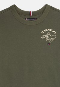 Olijfgroen t-shirt met ronde hals met de tekst "Avontuur bij Camp Tommy" en een graphic van gekruiste peddels op de linkerborst, met het Tommy Hilfiger-logo.