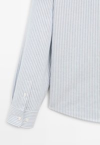 Camicia a righe in cotone azzurro chiaro e bianco, con maniche lunghe, polsini con bottone e orlo curvo. Tessuto testurizzato con strisce verticali.
