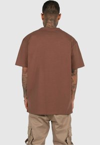 T-shirt marron à manches courtes en tissu doux, avec une coupe décontractée. L'arrière est uni, sans graphiques ni motifs.