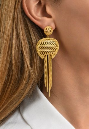 Les boucles d'oreilles pendantes en ton doré présentent un design géométrique texturé avec un sommet circulaire et des chaînes allongées, créant un effet de cascade.