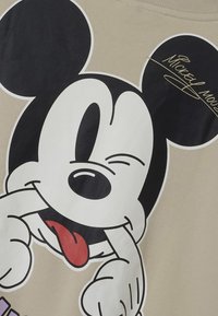 Graafiline T-särk, millel on suur mustvalge Mickey Mouse'i disain heledal beežil taustal, punase keele ja autogrammi detailiga.
