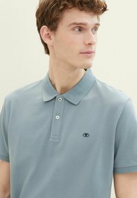 Polo shirt bleu clair en coton texturé, doté d'un col, d'une patte de boutonnage à trois boutons et d'un petit logo brodé sur la poitrine.