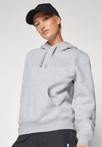 Felpa grigia con tasca frontale, cappuccio con stringhe e logo "BJORN BORG" in rosa. Abbinata a un cappellino nero con iniziali in rilievo.