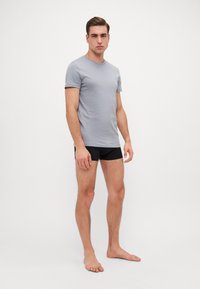 T-shirt gris à manches courtes en tissu doux, associé à un boxer noir. La coupe est près du corps avec un encolure ronde.