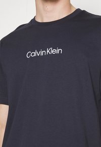 Námořnická modrá bavlněná trička s bílým logem "Calvin Klein". Krátký rukáv a design s kulatým výstřihem, s hladkou a jemnou texturou.
