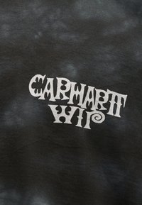 Μαύρο ύφασμα με λευκό στιλιζαρισμένο κείμενο που γράφει "CARMADETH WIP" σε κυματιστή, καλλιτεχνική γραμματοσειρά.