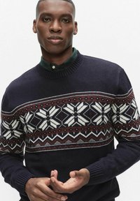 Granatowy sweter dzianinowy z wzorzystym karczkiem, na którym znajdują się białe płatki śniegu i bordowe akcenty. Okrągły, prążkowany dekolt i mankiety; miękka tekstura.