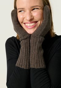 Gants en tricot côtelé marron fabriqués à partir d'un matériau doux, avec une finition texturée. Les gants sont portés avec les mains placées sur le visage.