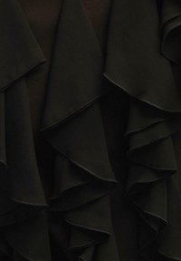 Juodas audinys, turintis sluoksniuotus, raukšlėtus kraštus su lygiu paviršiumi. Raukšlės turi kontrastingas siūles, kurios pagerina dizainą.