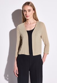 Ljusbeige kort kavaj i texturerad tyg, med V-ringning och trekvartslånga ärmar, bärs över en svart topp.