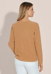Bruine geribbelde trui met een ronde halslijn en lange mouwen, voorzien van decoratieve stiksels op de schouders. Gepaard met witte jeans.