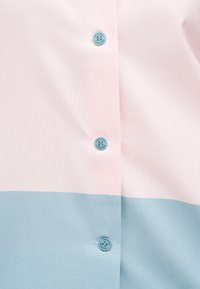 Κοντινό πλάνο υφάσματος με ροζ και μπλε μπλοκ χρωμάτων, με τρία μικρά μπλε κουμπιά σε κάθετη ευθυγράμμιση.