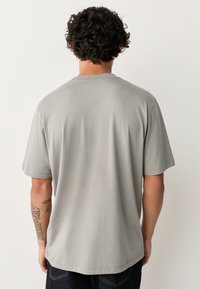 Grey cotton t-shirt featuring a relaxed fit, short sleeves, and a round neckline. Back view displays a smooth texture and simple design.