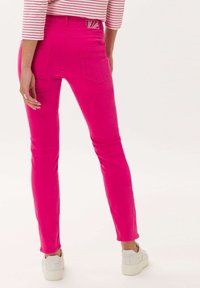 Pantalones ajustados rosa con bolsillos traseros y detalles de costura, combinados con zapatillas blancas. El material parece ser denim o una tela similar.