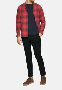 Czerwona i czarna koszula w kratę na guziki noszona na granatowej koszulce, w połączeniu z czarnymi spodniami i brązowymi zamszowymi sneakersami z szarymi akcentami.