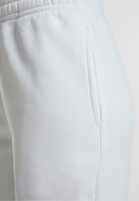 Lichtblauwe trainingsbroek van zacht materiaal heeft een elastische tailleband en een zijvak met een gladde textuur.