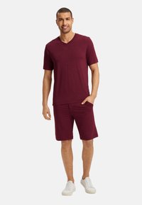 Maglietta bordeaux a V abbinata a pantaloncini coordinati, realizzati in un tessuto morbido. Indossata con sneakers bianche, presenta una vestibilità comoda e tasche.