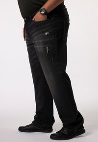 Vaqueros de mezclilla negros con un corte relajado, con rayas descoloridas y detalles desgastados. Combinados con zapatos negros y un reloj de pulsera.