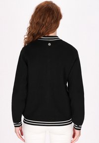 Zwarte gebreide trui met witte gestreepte ribbelmanchetten en tailleband, met een ronde kraag en een klein logo-detail bij de achterkant van de halslijn.