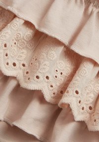 Un tissu rose clair avec des volants superposés ornés de motifs floraux brodés et de découpes en œillet le long des bords, mettant en valeur la texture et le détail.