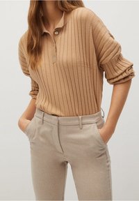 Polo en maille côtelée marron clair avec une patte de boutonnage à trois boutons, associé à un pantalon beige clair sur mesure avec poches latérales.