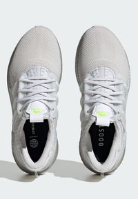 Białe buty sportowe z siateczkową cholewką, z teksturowanym wzorem, elastycznym systemem sznurowania i zielonym logo na języku. Gumowa podeszwa.