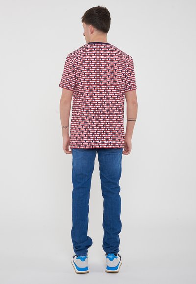 Camicetta a maniche corte rossa e bianca con motivo e testo, abbinata a jeans blu e sneaker bianche con dettagli blu.