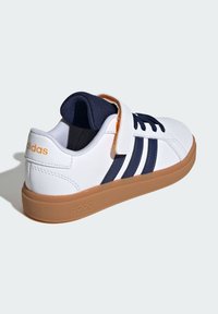Zapatillas Adidas con una parte superior sintética blanca, rayas navy y una suela de goma marrón. Incluyen una banda de velcro para el cierre.