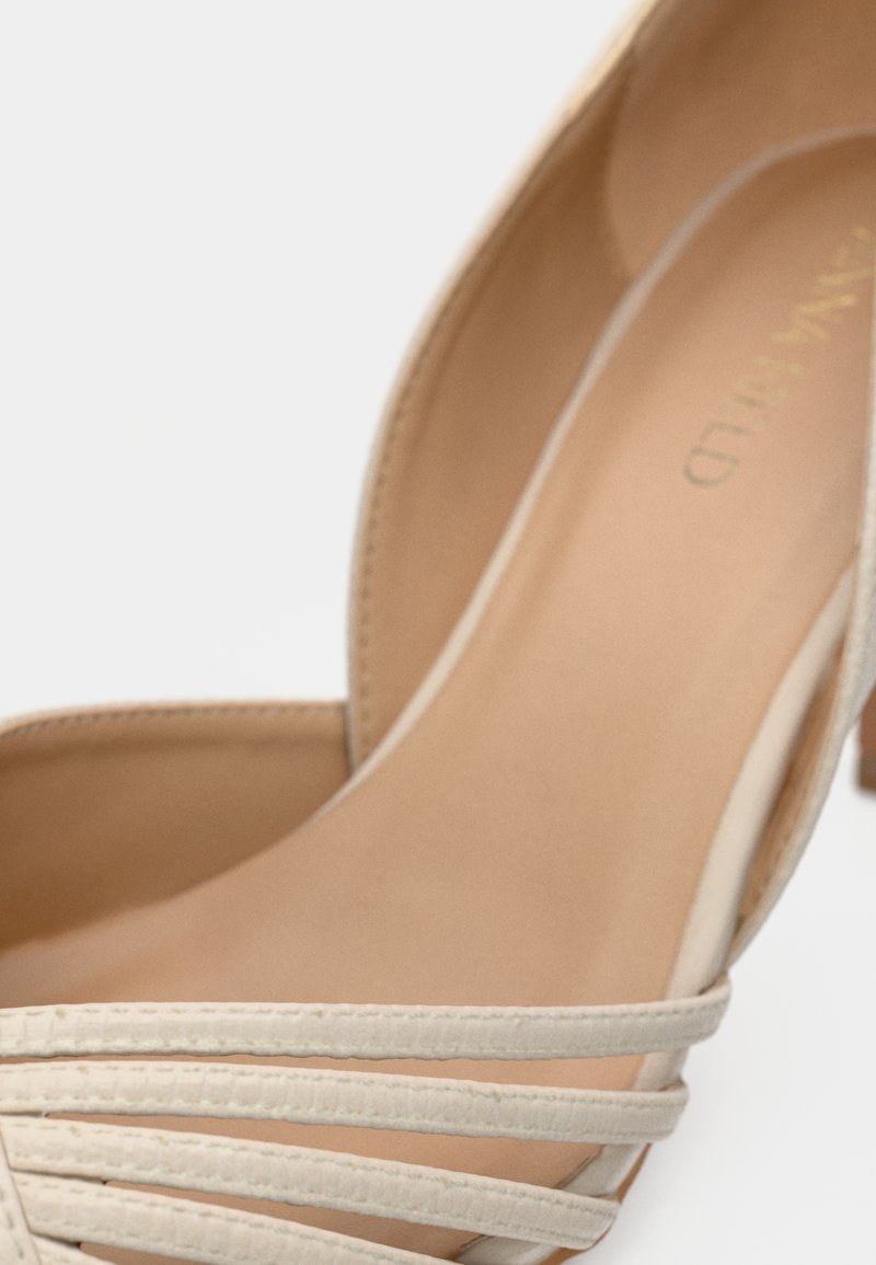 Zapato de tacón alto beige con parte superior de cuero suave, con correas verticales y puntera redondeada. La plantilla es de color marrón claro con un acolchado mínimo.