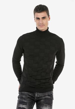 Schwarzer Rollkragenpullover mit einem strukturierten Gewebemuster, gerippten Bündchen und Saum. Kombiniert mit zerrissenen schwarzen Jeans.