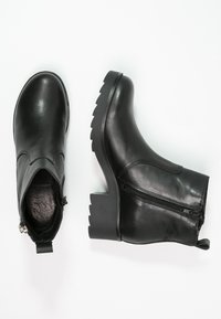 Botas de cuero negro hasta el tobillo con superficie texturizada, tacón grueso, cremallera lateral y diseño de punta redondeada. Suela plana con un patrón de banda de rodadura.