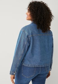 Giacca di jeans azzurro chiaro, con una vestibilità rilassata, chiusura a bottoni e superficie testurizzata, abbinata a pantaloni di jeans coordinati.