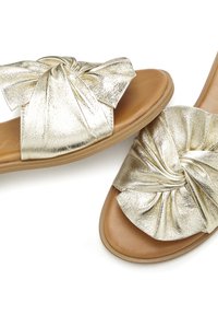Gold metallic slide sandals featuring a twisted bow design, smooth texture, and a tan footbed with a flat sole.