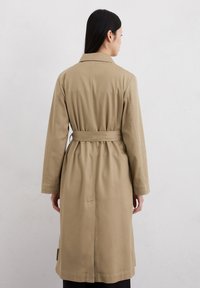 Cappotto trench beige con vita cintrata, maniche lunghe e colletto; presenta una texture liscia e un design a taglio diritto.