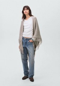 Light gray fringed shawl in a textured knit, worn over a white T-shirt and blue jeans. Brown shoes complete the outfit.