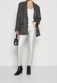Blazer texturizado en blanco y negro, camiseta blanca de tirantes, pantalones plateados brillantes, botas de tacón negras, bolso pequeño negro.