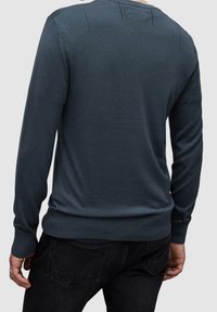 Man wearing dark blue long-sleeve sweater and black jeans, shown from the back against plain light background.