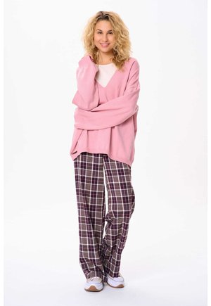 Helle rosa, übergroße Sweater mit V-Ausschnitt, kombiniert mit lässigen, karierten Schlafanzughosen in dunklem Purpur, Weiß und grünen Farbtönen. Weiße Sneakers runden den Look ab.