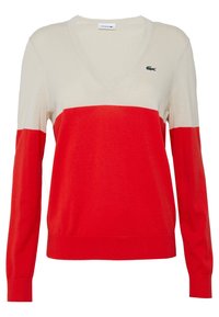 Červený a krémový svetr s výstřihem do V, vyrobený z měkkého materiálu, s dlouhými rukávy a horizontálním designem v blokových barvách. Logo Lacoste umístěné na hrudi.