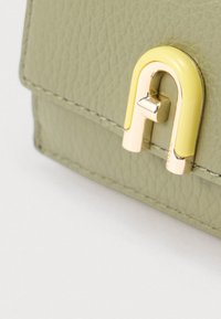 Zaļa ādas maks ar dzeltenu un zeltainu metāla aizdari. Virsma ar tekstūru, taisnstūrveida forma un šūtas detaļas.