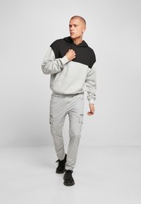Felpa color block grigia e nera con tasca a marsupio; pantaloni cargo grigi chiari con tasche e scarpe nere stringate.