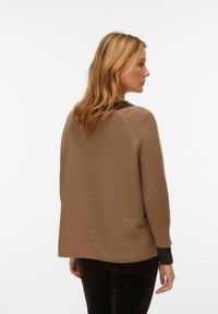 Bruine geribde trui met een losse pasvorm en een contrasterende donkere kraag. Gladde textuur, lange mouwen en een afgeronde zoom.