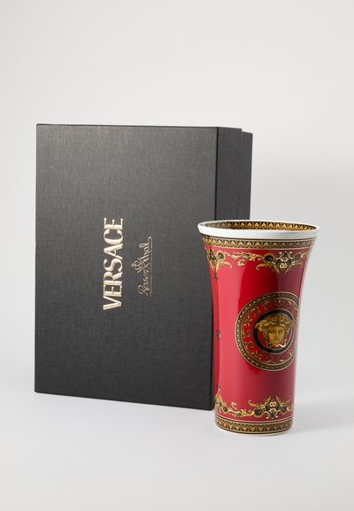 Czerwony ceramiczny wazon ze złotymi zdobieniami i centralnym motywem Meduzy, w kształcie rozszerzającej się filiżanki. Towarzyszy mu czarne, teksturowane pudełko.