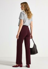 Grå kortærmet t-shirt, bordeaux højtaljede bukser, blanke røde sko og en vævet sort håndtaske. Glat stof og skræddersyet pasform.