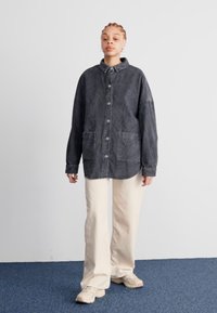 Hnedá hrubá kordúrová košeľa s klopovým golierom, prednými gombíkmi, dvoma náprsníkmi, kombinovaná s krémovými širokými nohavicami.