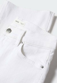 Jean en denim blanc plié avec poche avant, bouton argenté, rivets et étiquette de taille MNG visible.